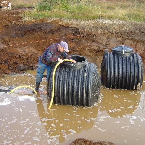 Jón er þarna að dæla vatni í brunnana til þess að þeir fljóti ekki upp.
Ef vel er að gáð má sjá appelsínugula línu rétt ofan við höfuðið á Jóni en hún sýnir vatnshæðina í tjörninni, uppistöðulóninu:)